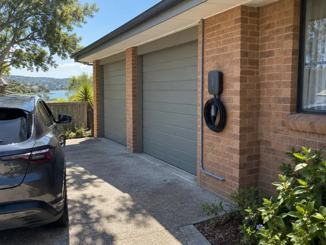 Wall-mounted EV charger on a brick exterior wall beside a double garage in Saratoga