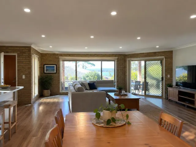 Living room with recessed downlights, brick walls, wood floor and large windows in Empire Bay