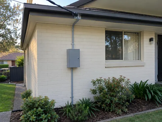 Exterior brick house with new overhead service cable and point-of-attachment bracket above a meter box in Bensville